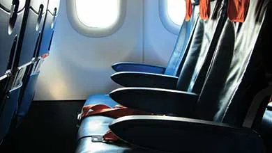 Empty row of dark blue airplane seats with orange accents, beside two bright windows.