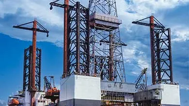 Offshore oil platform with steel lattice towers and cranes under a cloudy sky.