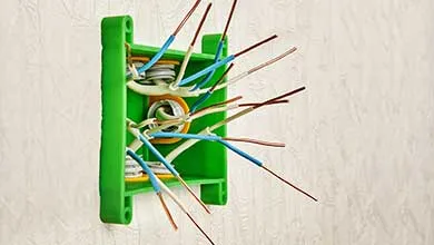 Green electrical junction box on a wall with protruding blue and white stripped wires.