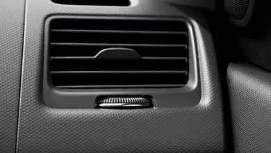 Close-up black and white image of a car’s rectangular air vent with horizontal slats and a small ridged control dial below.