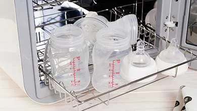 Clean baby bottles and nipples on a metal rack extend from a white sterilizer.