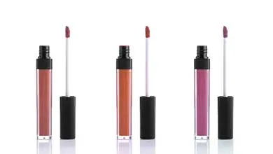 Three open tubes of liquid lipstick with their applicators are arranged in a row, showing shades of dusty rose, orange, and magenta on a white background.
