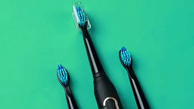 A black electric toothbrush with two blue-bristled replacement heads on a green background.