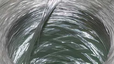 Close-up of translucent thermoplastic composite fibers wound into a tight coil, showing layered strands and texture.