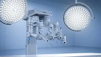A multi-armed surgical robot in a modern operating room, lit by two large circular surgical lights.