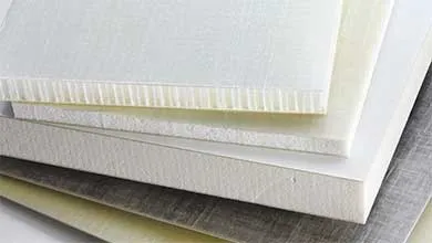 Close-up of stacked composite panels in white, beige, and grey, showing different textures and thicknesses. The top panel's edge reveals a honeycomb core.