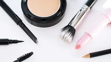 Assorted makeup items—foundation, brush, pink lipstick, mascara, and eyeliners—arranged on a white background.