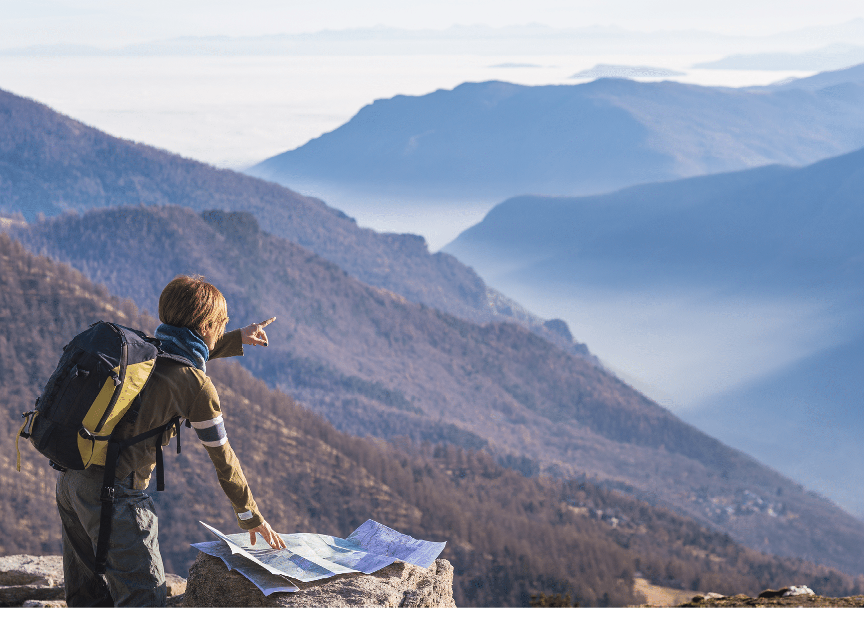 Female hiker with backpack reading trekking map while pointing finger to the mountains on the italian Alps  Mist and fog in the valley below, larch and pine tree forest around  Selective focus 